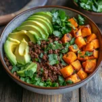 "Viral Ultimate Ground Beef Sweet Potato Bowl topped with avocado slices and cilantro, served in a rustic bowl."
